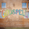 A curtain warmer of a brick building with windows and the Godspell logo in rainbow lettering